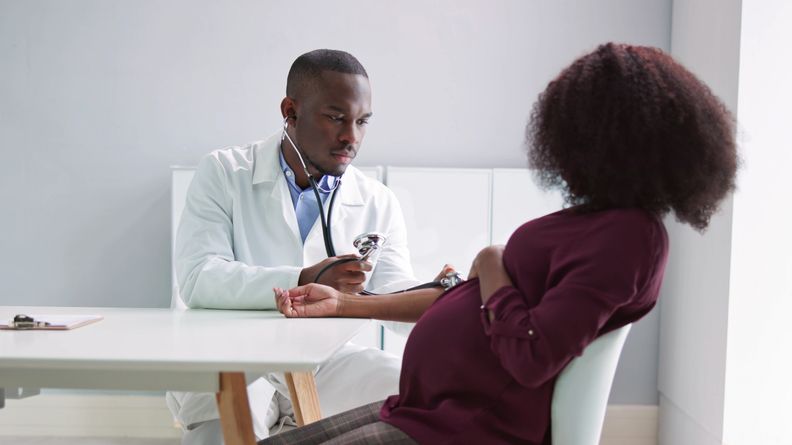 Stock photo of a male doctor measuring the blood pressure of a pregnant patient in a clinic
