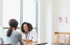 A happy mid-adult female cardiologist smiles as she listens to a female patient