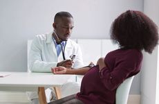 Stock photo of a male doctor measuring the blood pressure of a pregnant patient in a clinic